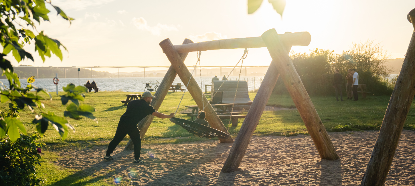 Far og barn gynger på legepladsen ved Ibæk Strand
