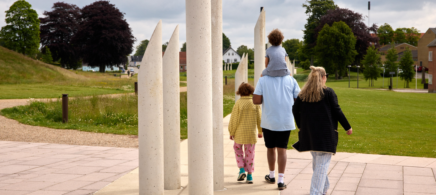 En familie går tur i monumentområdet i Jelling ved palisaderne