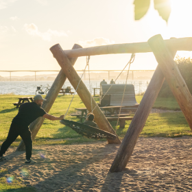 Far og barn gynger på legepladsen ved Ibæk Strand