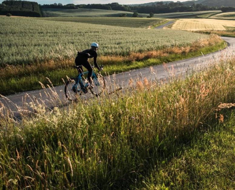 En person cykler på racercykel på landevejen langs åbne marker i Vejle