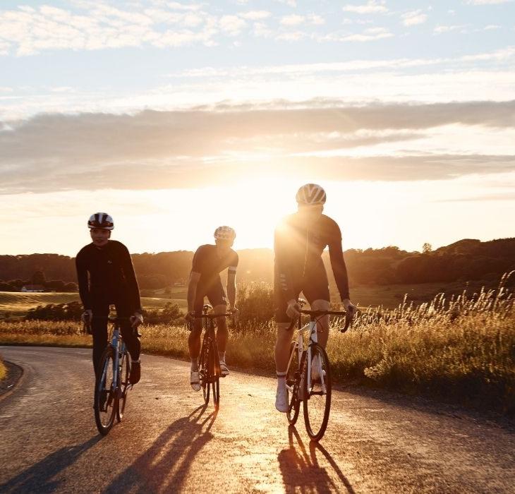 Tre landevejsryttere på cykeltur ved Jelling i solnedgangen