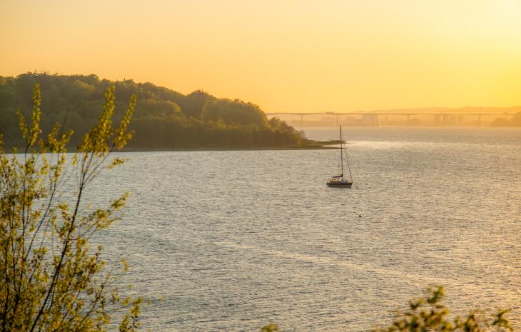 Vejle Fjord set fra Andkær Vig i solnedgang med en båd på fjorden og Vejlefjordbroen i baggrunden